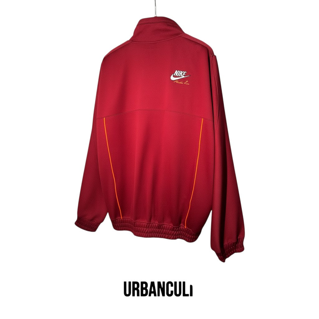 Giacca sportiva Nike x Martine Rose rosso scuro in tessuto tecnico con logo co-branded e dettagli arancioni.